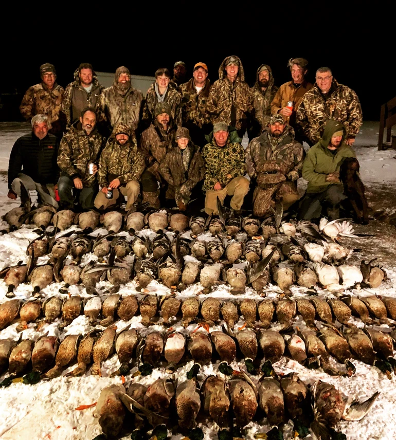 Group of hunters posing at night behind a large spread of harvested ducks during a guided North Dakota hunt